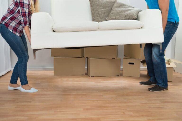 Happy Young Couple Carrying Couch In New Home